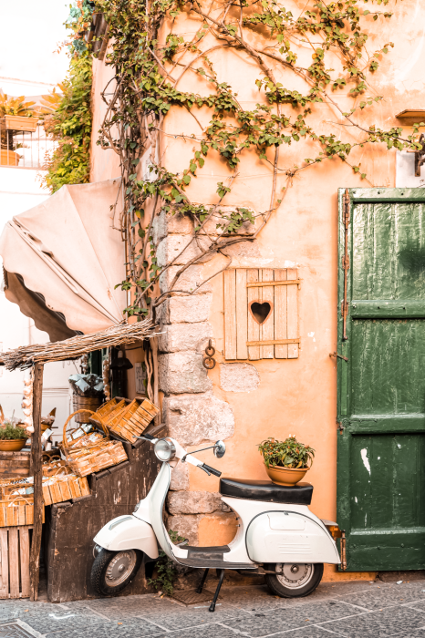 Poster  Un scooter blanc avec un bâtiment recouvert de vigne en arrière-plan